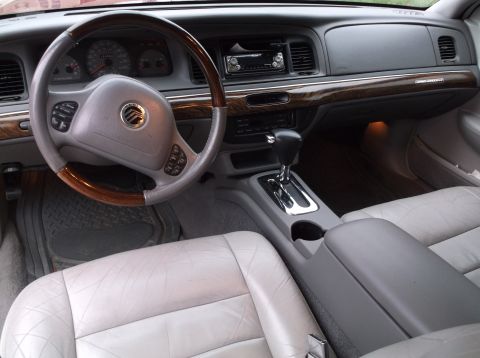 1999 Mercury Grand Marquis - The interior of a 1999 Mercury Grand Marquis is shown, featuring a wood-trimmed steering wheel, dashboard with a radio, and light-colored l…