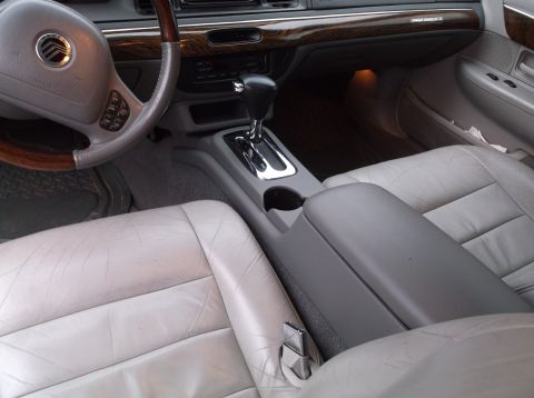 1999 Mercury Grand Marquis - The interior of a 1999 Mercury Grand Marquis shows the steering wheel, center console with gear shifter, and light-colored leather seats. T…