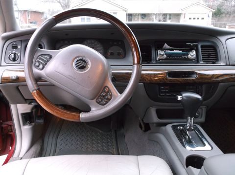 1999 Mercury Grand Marquis - The interior of a 1999 Mercury Grand Marquis is shown, featuring a wood-trimmed steering wheel and dashboard, a center console with a gear…
