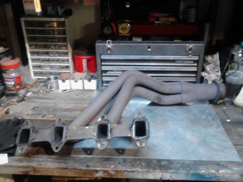 1973 Ford F-250 - A set of exhaust headers is laid out on a workbench with various tools and storage containers in the background. The headers appear to be m…