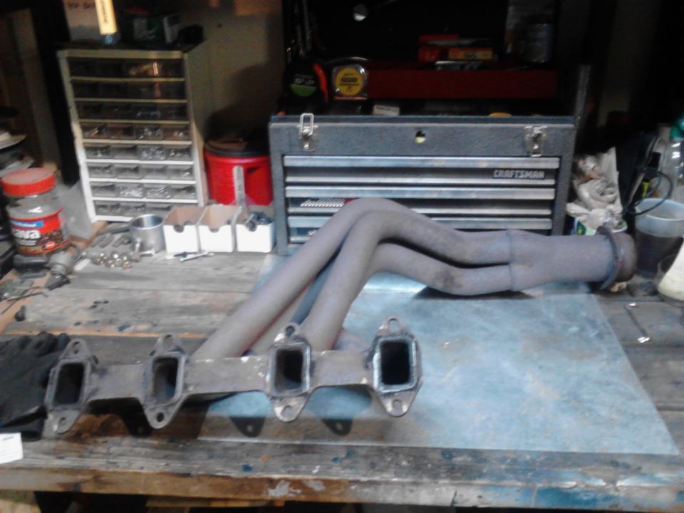 Exhaust headers on a workbench with tools and storage in the background.