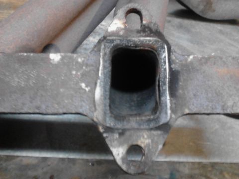1973 Ford F-250 - A close-up view of a rusty, square exhaust pipe flange with two bolt holes. The flange appears to be part of a vehicle's exhaust manifold.