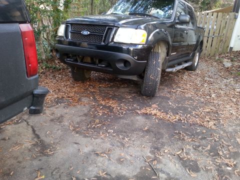 2001 Ford Explorer - The front quarter view of a black Ford Explorer Sport Trac pickup truck is shown parked on a gravel and asphalt surface covered in fallen l…