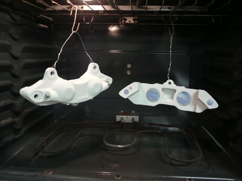 Two white brake calipers hanging in an oven