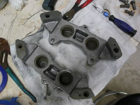 Two gray brake caliper assemblies on a white towel with tools.