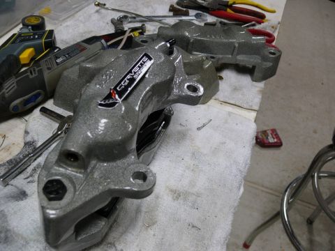 Two gray painted brake calipers with a Corvette Stingray sticker and tools.