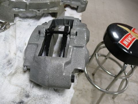 Gray painted brake caliper with black brake pads on white cloth, chrome stool nearby.