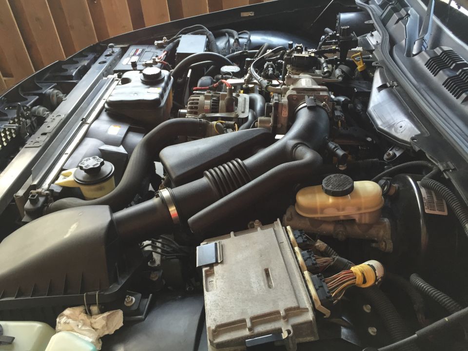 Close-up of a car engine bay showing air intake, battery, brake fluid reservoir, and ECU.