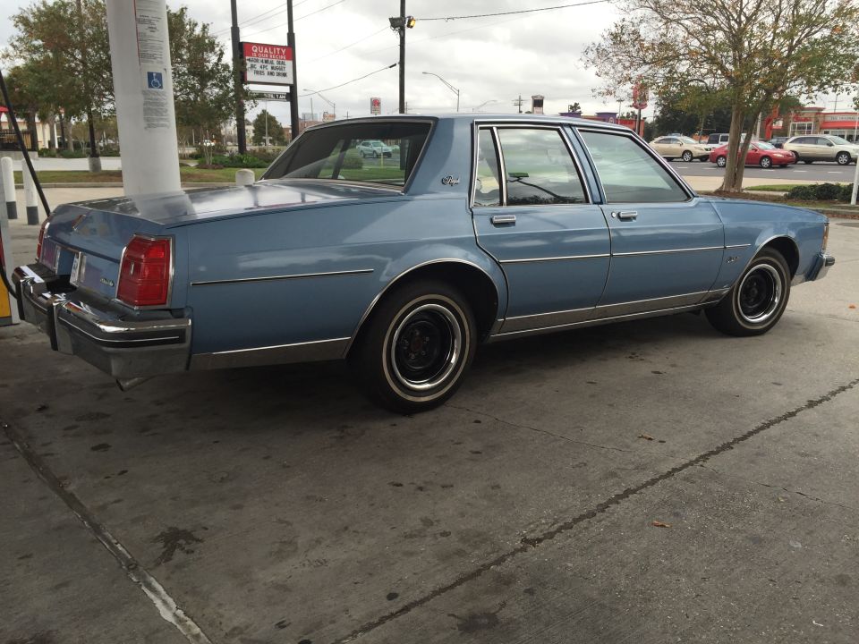 Light blue sedan parked at a gas station, rear passenger side view.