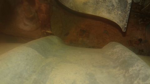 1996 Ford Bronco - The underside of a vehicle's chassis is visible, showing rusty metal components and a curved, light-colored surface that appears to be part…