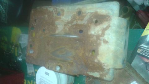 1996 Ford Bronco - A heavily rusted metal bracket with multiple bolt holes is shown in a cluttered setting. The bracket appears to be a vehicle part, possibly…