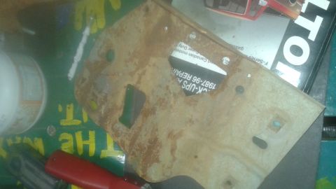 1996 Ford Bronco - A rusty metal bracket with a sticker that reads "CK-UPS H. 1987-96 REPAIR" is placed on a green surface with yellow lettering that says "TH…