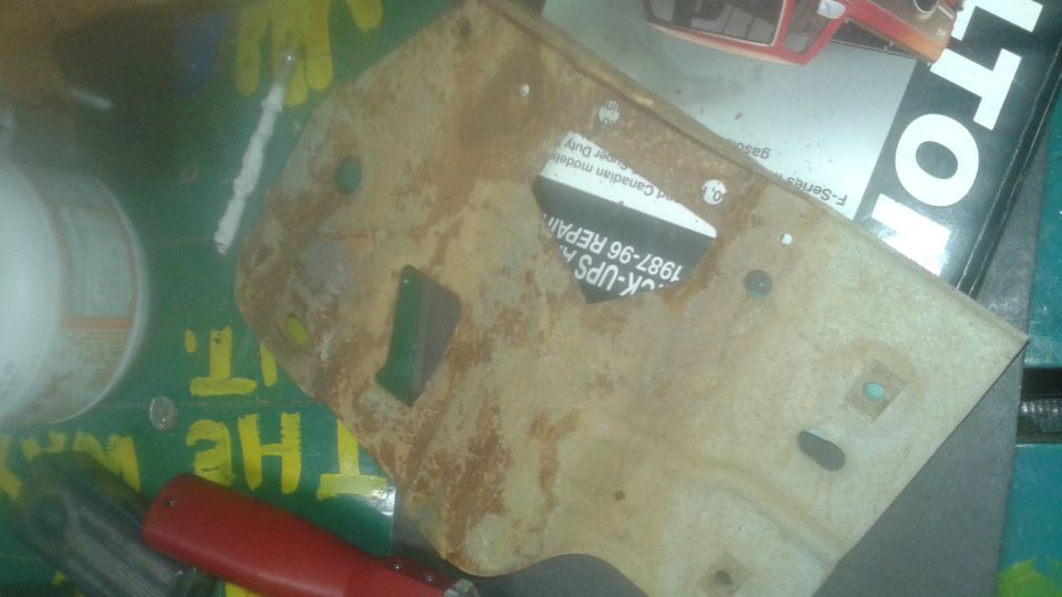 Rusty metal bracket with text sticker on green surface with yellow lettering.