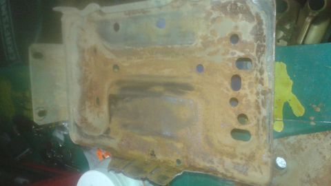 1996 Ford Bronco - A heavily rusted metal bracket with multiple circular and oval holes is shown. The bracket appears to be part of a vehicle's undercarriage…