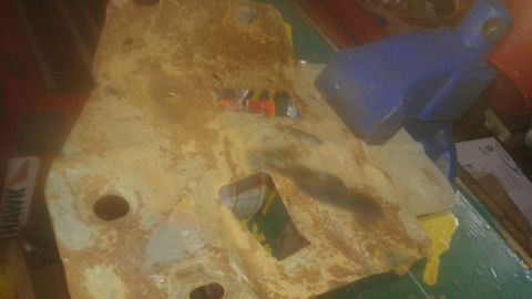 1996 Ford Bronco - A rusty, yellow-painted metal part with a rectangular cutout is held by a blue vise. A yellow liquid is dripping from the metal part onto a…