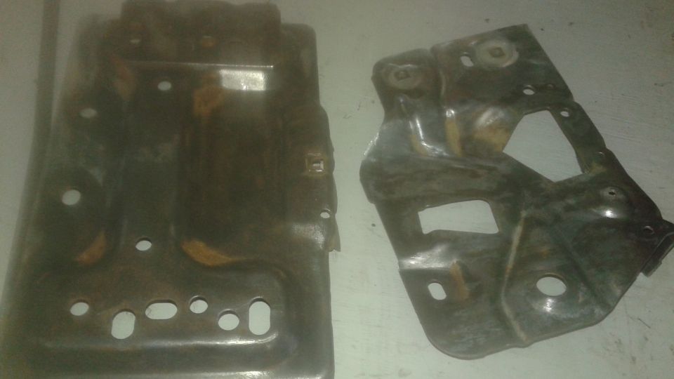 Two rusty metal automotive parts on a light surface.