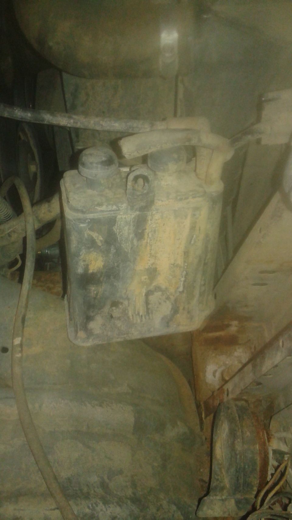 Underneath view of a dirty plastic reservoir with a black cap and a hose.
