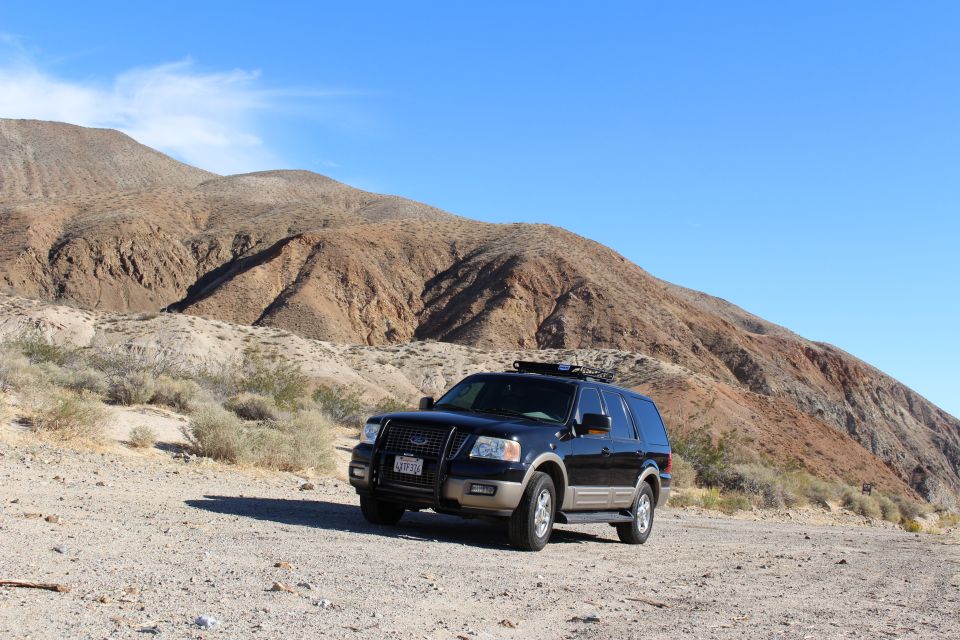 Black Ford Expedition SUV parked on a dirt road in a desert with mountains.