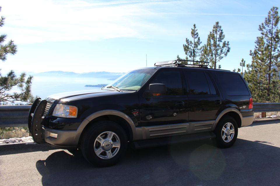 Black Ford Expedition SUV with brush guard parked by a lake.