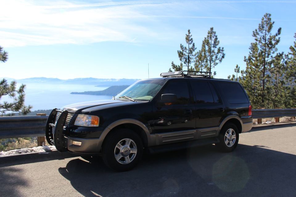 Black Ford Expedition SUV with brush guard and roof rack parked by a lake.