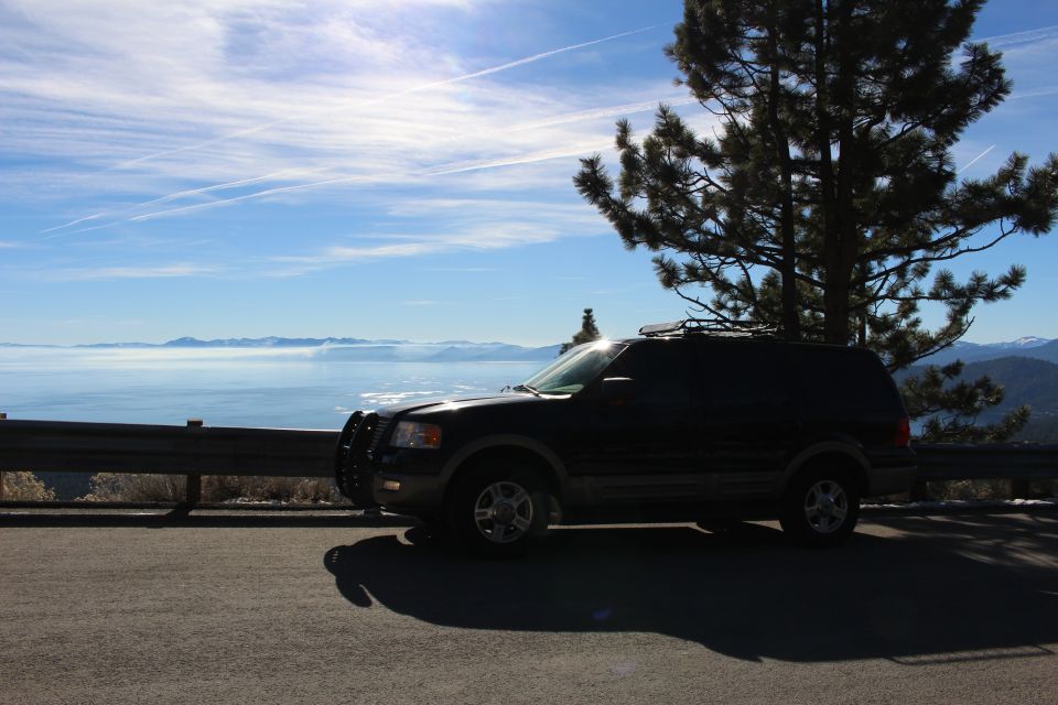 Dark SUV parked on a scenic overlook with a large body of water and mountains in the background.