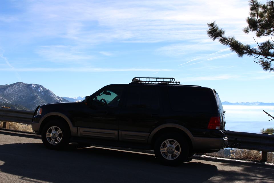 Black Ford Expedition SUV parked on a scenic overlook with mountains and a lake.