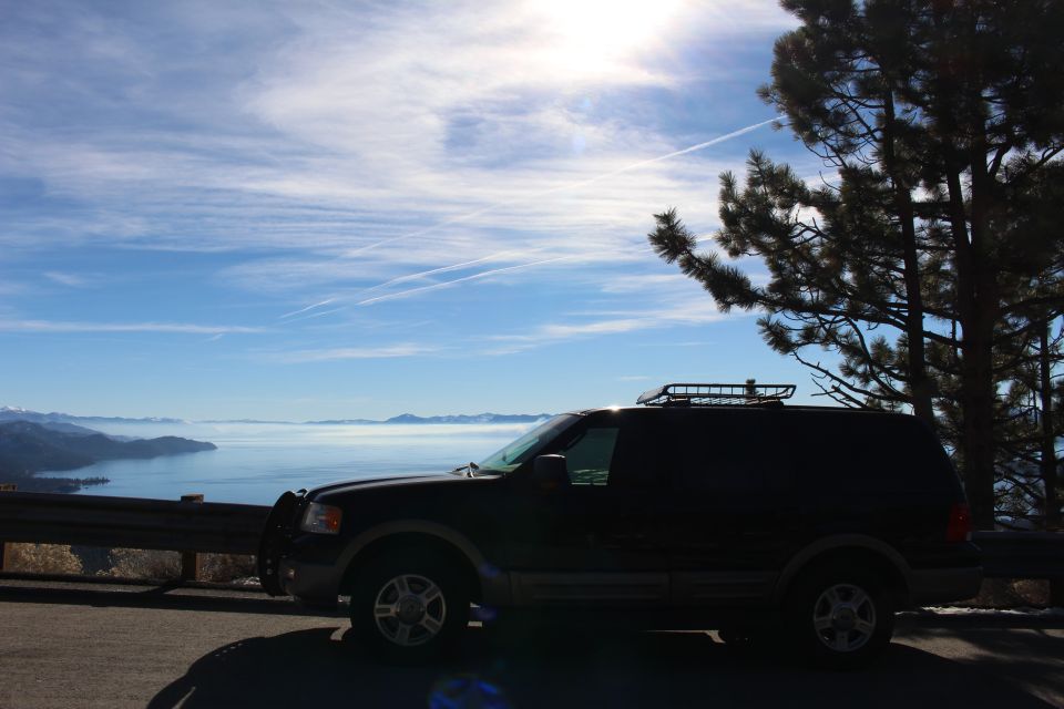 Dark SUV parked on a scenic overlook with a lake and mountains in the background.