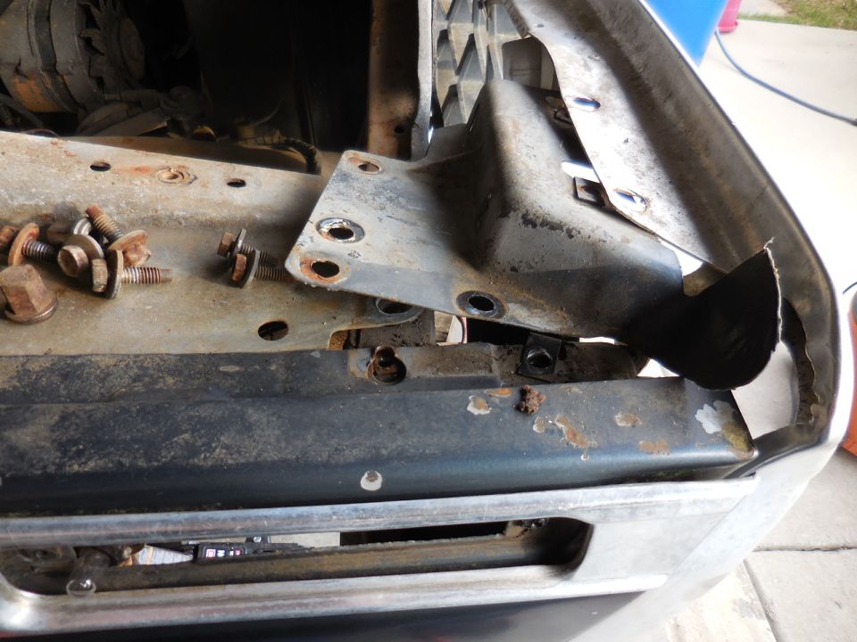 Loose bolts and brackets on a vehicle's front end, showing disassembled parts near the grille