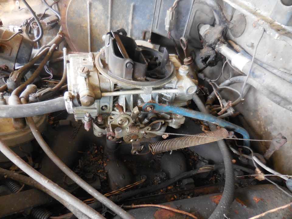 Close-up of a carburetor with hoses and wiring in an engine bay
