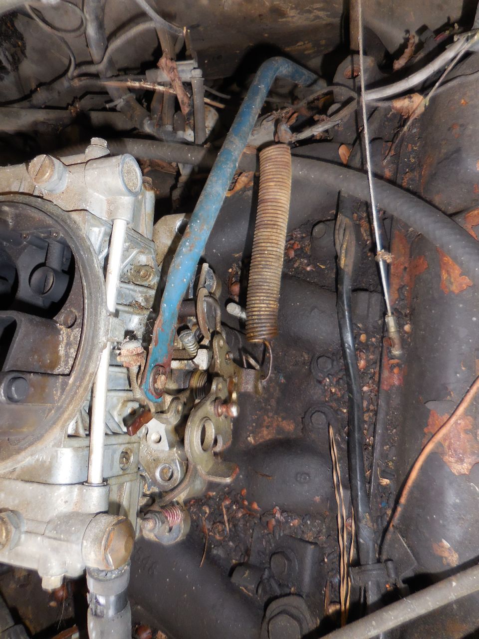 close-up of carburetor linkage with a blue rod and a large spring