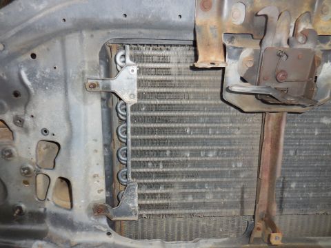 1979 Ford Bronco - Close-up of a vehicle's radiator and hood latch assembly, showing metal components and cooling fins.