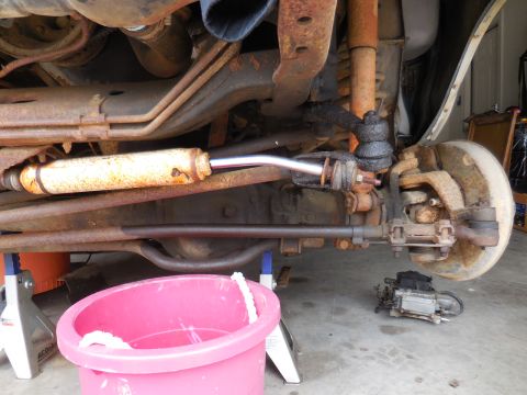 1979 Ford Bronco - Underneath view of vehicle's steering and suspension system, showing various rusty parts and a pink bucket.