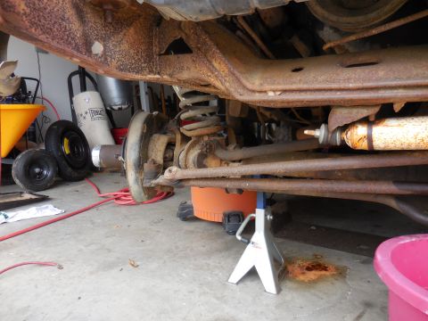 1979 Ford Bronco - The heavily rusted undercarriage of a vehicle is shown, supported by jack stands in a garage.