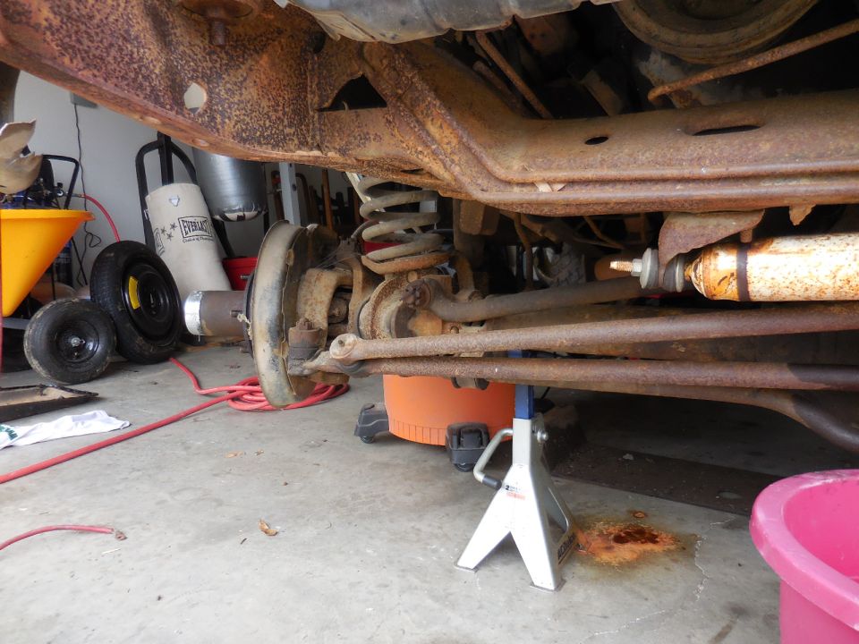 rusted frame, suspension, and brake components of a vehicle on jack stands