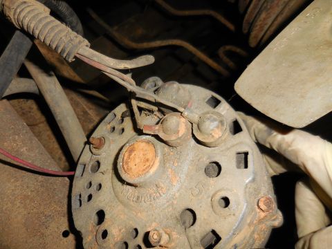 1979 Ford Bronco - A close-up view of a dusty and corroded automotive alternator with visible wiring and a gloved hand near the fan shroud.