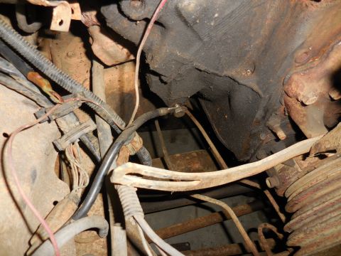 1979 Ford Bronco - A close-up view of the engine bay of a 1979 Ford Bronco, showing various hoses, wires, and engine components covered in grease and rust.