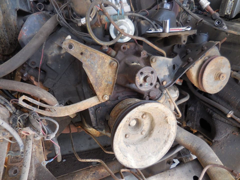 Rusty V8 engine with pulleys, brackets, hoses, and wiring.