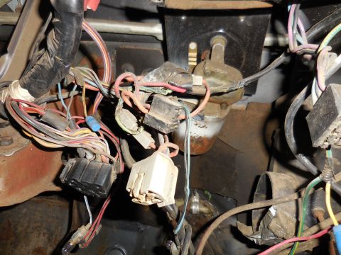 1979 Ford Bronco - A close-up view of a tangled mess of automotive wiring harnesses, connectors, and a small light bulb, likely located under the dashboard of…