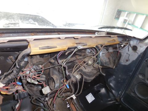 1979 Ford Bronco - The interior of a classic vehicle's dashboard area shows a complex wiring harness and exposed components under the windshield. A tan protec…