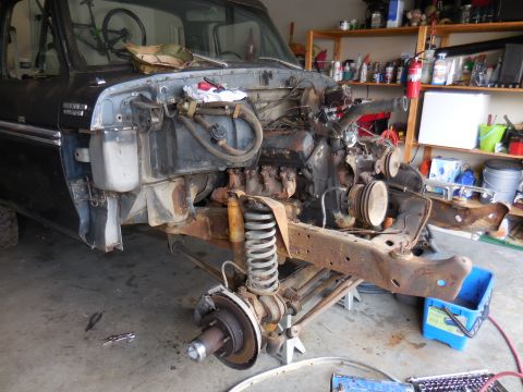 1979 Ford Bronco - The front end of a dark-colored Ford Bronco is disassembled in a garage, with the engine and front suspension components removed and restin…