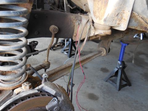 1979 Ford Bronco - The underside of a vintage vehicle, likely a 1979 Ford Bronco, is shown supported by jack stands. Visible components include a large coil s…