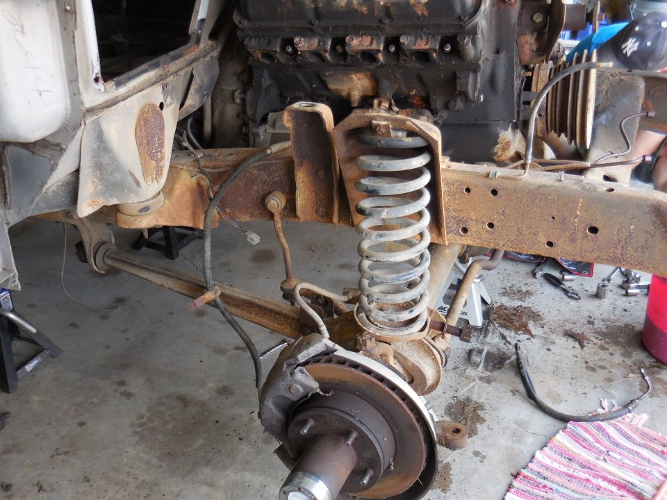 Rusty vehicle chassis with engine block and suspension components, viewed from the front