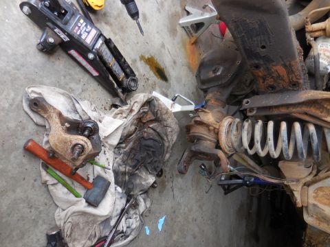 1979 Ford Bronco - Vehicle suspension parts, including a differential and coil spring, are laid out on the floor with tools and a jack.