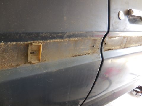 1979 Ford Bronco - A close-up view of a car's side panel shows a damaged trim clip and evidence of rust.