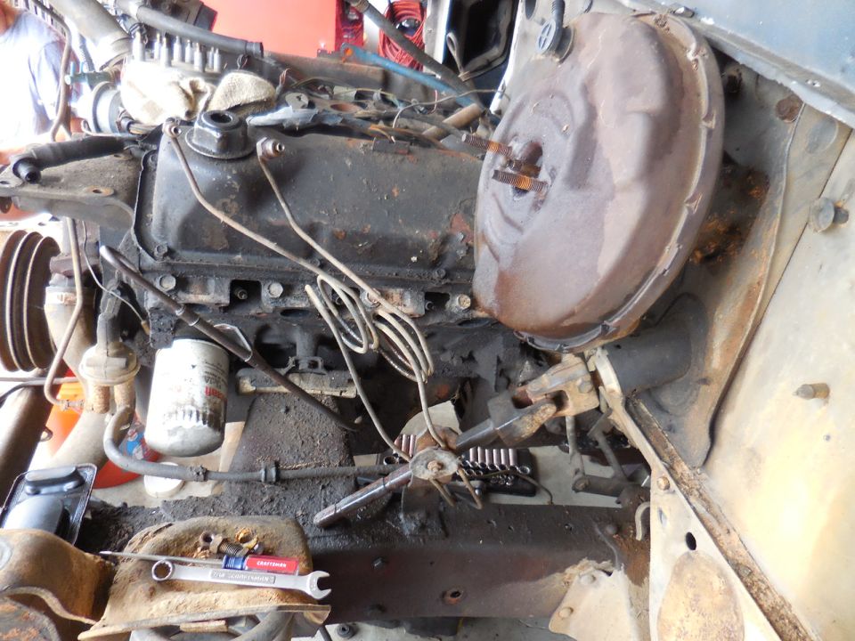 Close-up of a dirty engine bay with tools, brake booster, and engine block.
