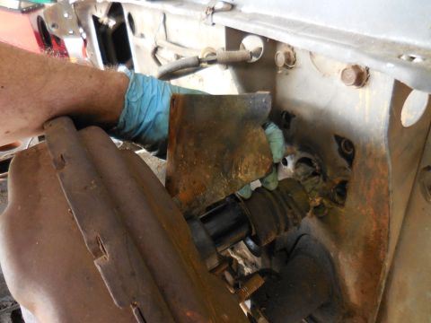 1979 Ford Bronco - A gloved hand is shown working on a rusty metal bracket attached to a vehicle's firewall, near a black rubber boot and a metal rod.