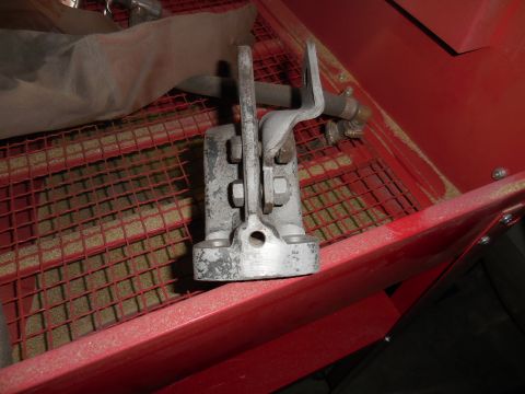 1979 Ford Bronco - A close-up view of a metal part with bolts and a hose fitting, resting on a red grate covered in sand. The part appears to be part of a san…