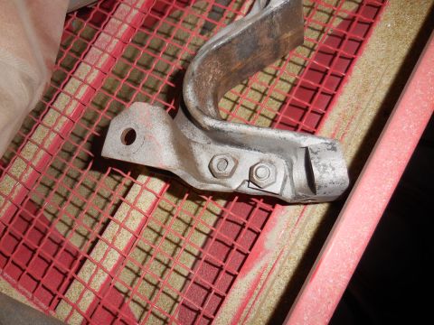 1979 Ford Bronco - A close-up shot shows a metal bracket with two bolts attached, resting on a red grid and sand.
