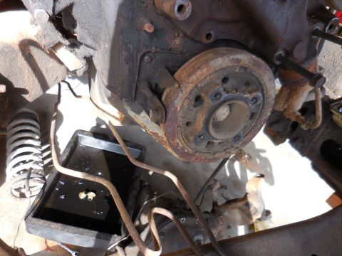 1979 Ford Bronco - A rusty engine crankshaft pulley is shown attached to a V8 engine block, with a black oil drain pan beneath it collecting fluid.