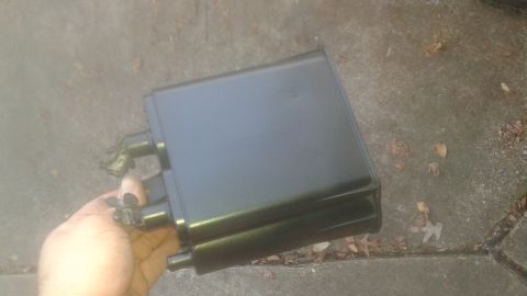 1996 Ford Bronco - A black rectangular part, possibly a charcoal canister, is held in a person's hand over a concrete surface with scattered leaves. The part…